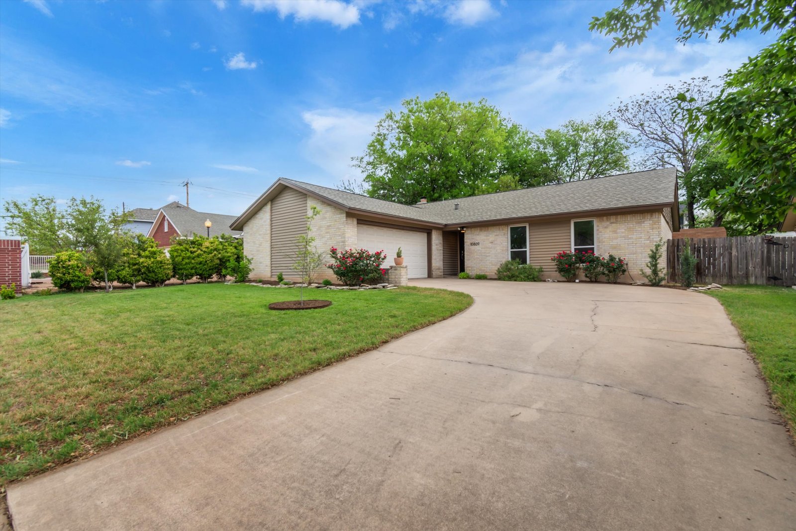 10809 Parkfield Dr front exterior — cream brick ranch with 2-car garage, rose bushes, and mature trees on a wide circular driveway