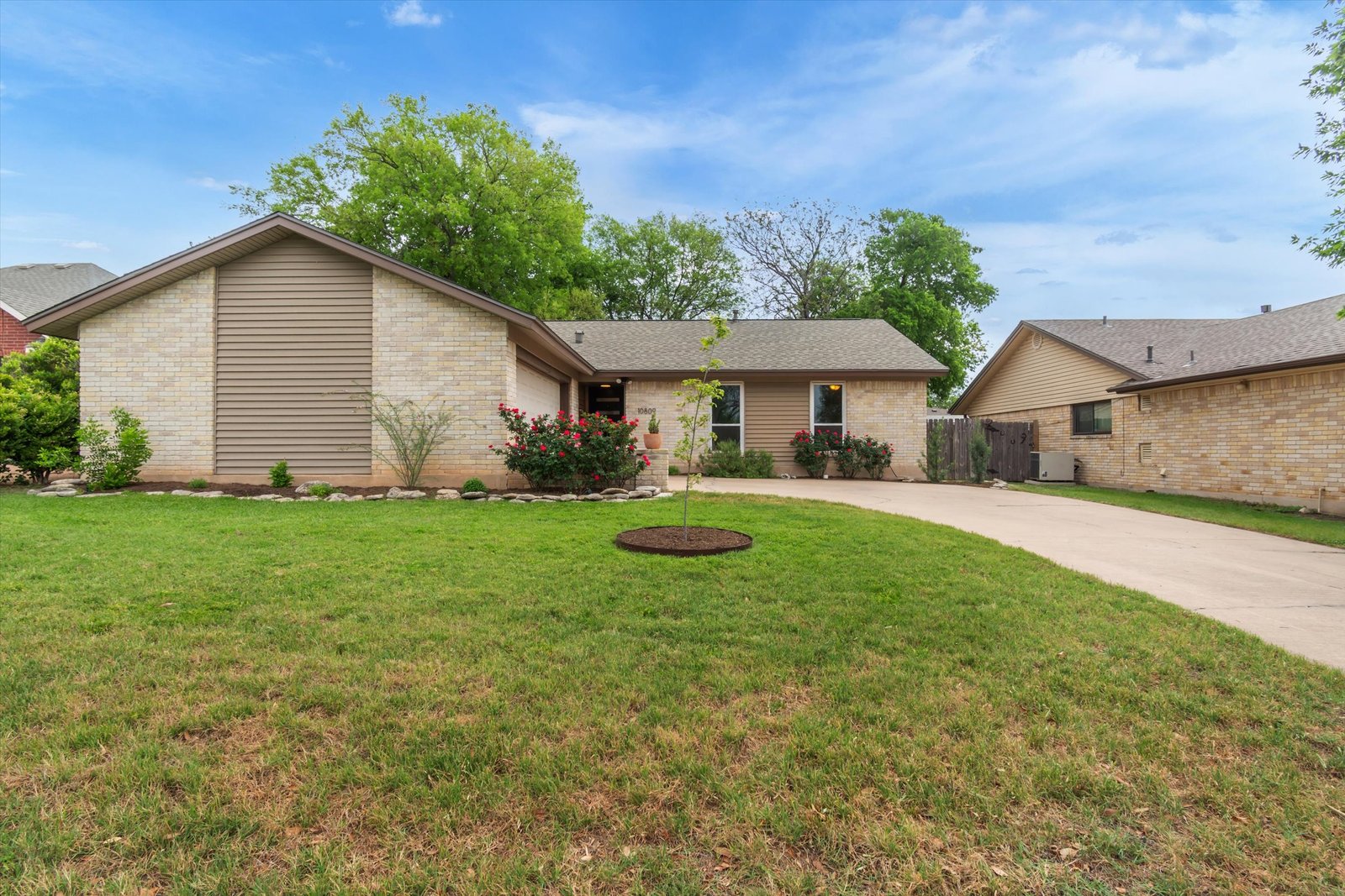 Angled view of 10809 Parkfield Dr showing cream brick and siding exterior, rose garden, and wide driveway
