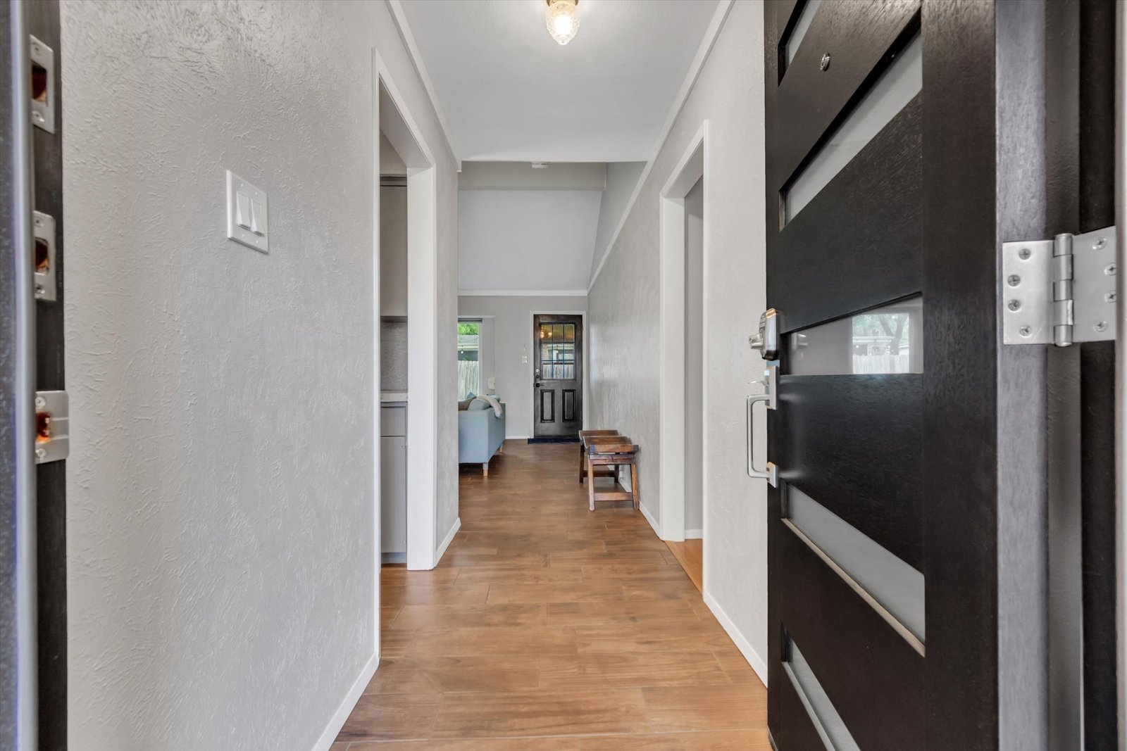 Entry hallway looking through to living room — modern black front door open, tile flooring, vaulted ceiling visible ahead