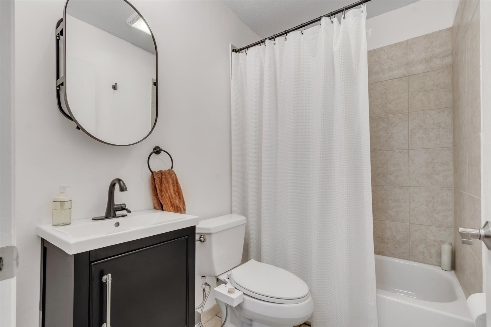 Second full bathroom — updated dark vanity with oval mirror, tile tub/shower surround, and modern fixtures