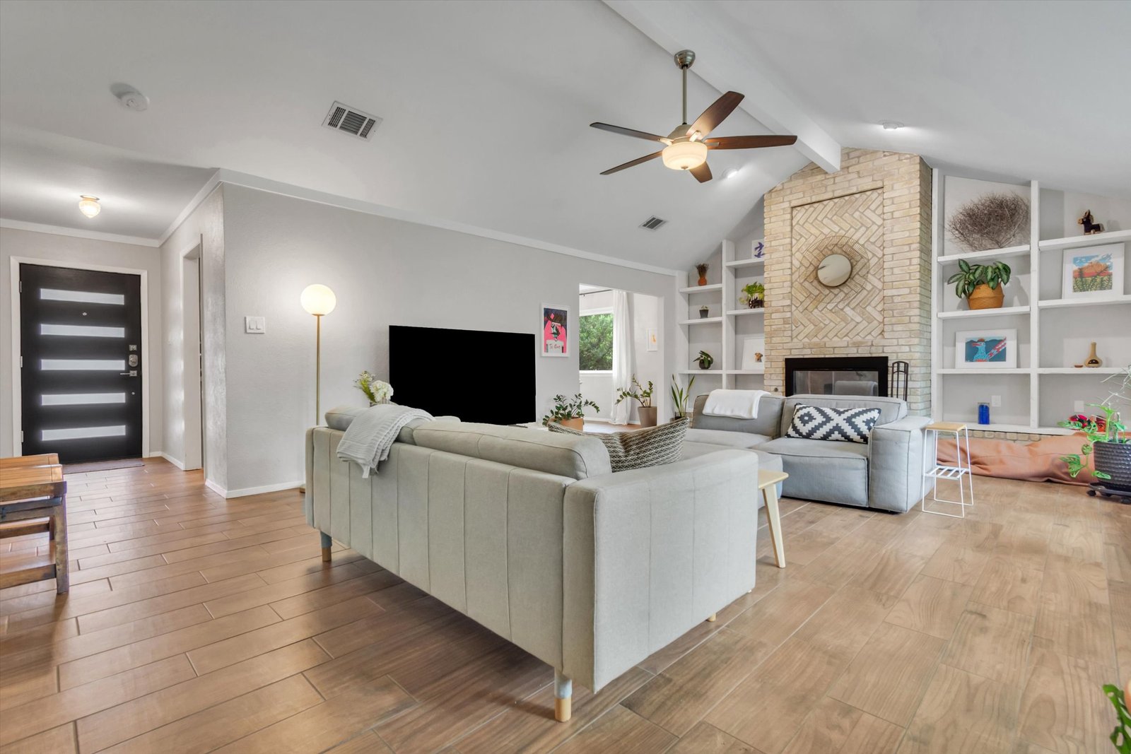 Open living area from dining room showing herringbone fireplace, built-in bookcases, front door, and spacious floor plan