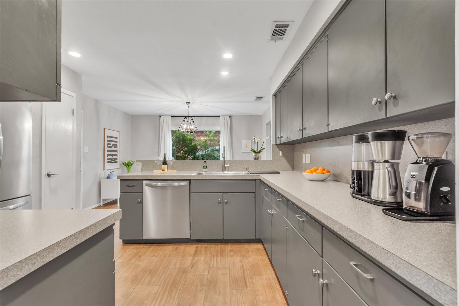 Kitchen looking toward dining room — stainless dishwasher, gray cabinets, counter space, geometric chandelier visible in dining area