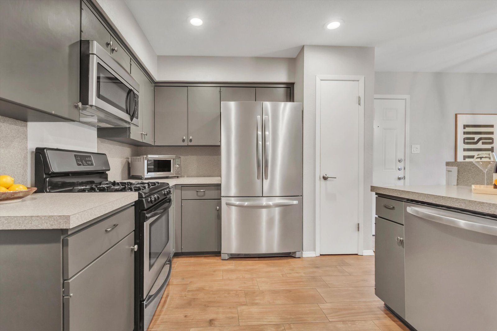Kitchen appliance wall — gas range, French door refrigerator, microwave, gray cabinets, and tile flooring