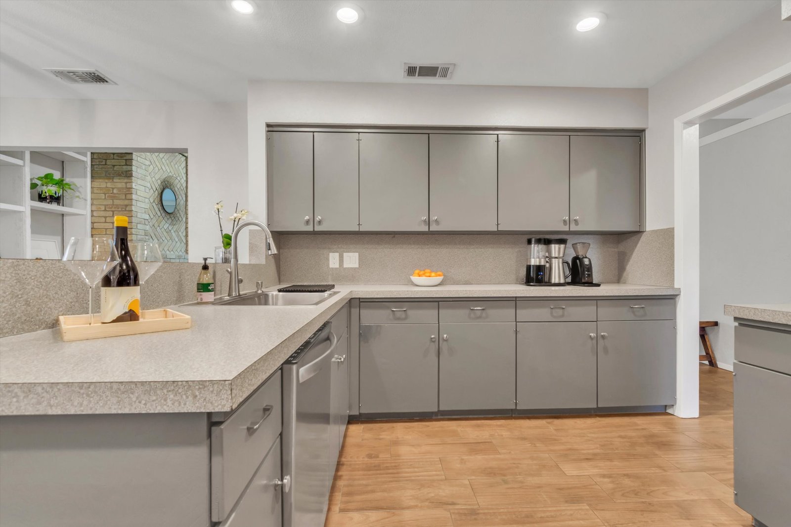 Kitchen with gray cabinets, counter space with sink, herringbone fireplace visible through pass-through window to living room
