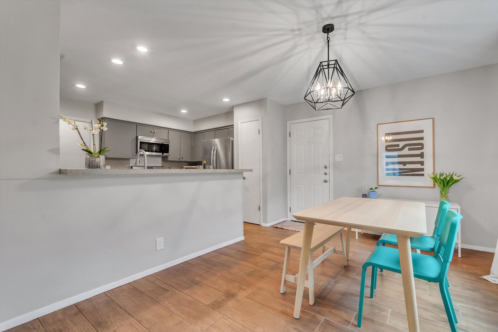 Dining area looking into kitchen through pass-through opening — breakfast bar, gray cabinets, stainless appliances visible