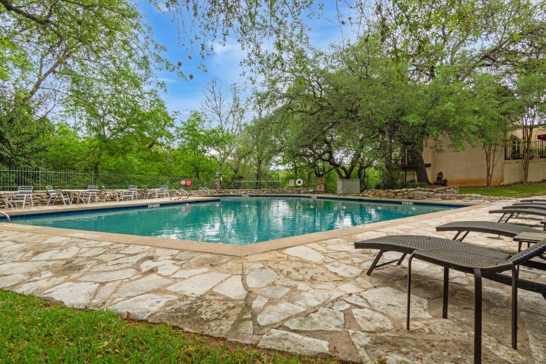 Stone pool deck with lounge chairs and mature shade trees