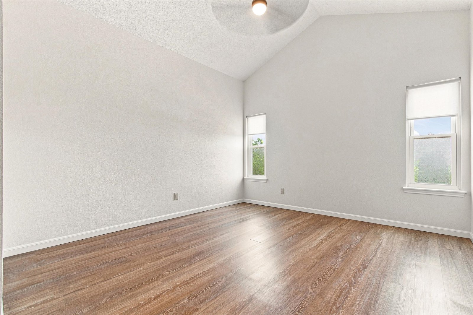 Primary bedroom with vaulted ceiling and wood floors