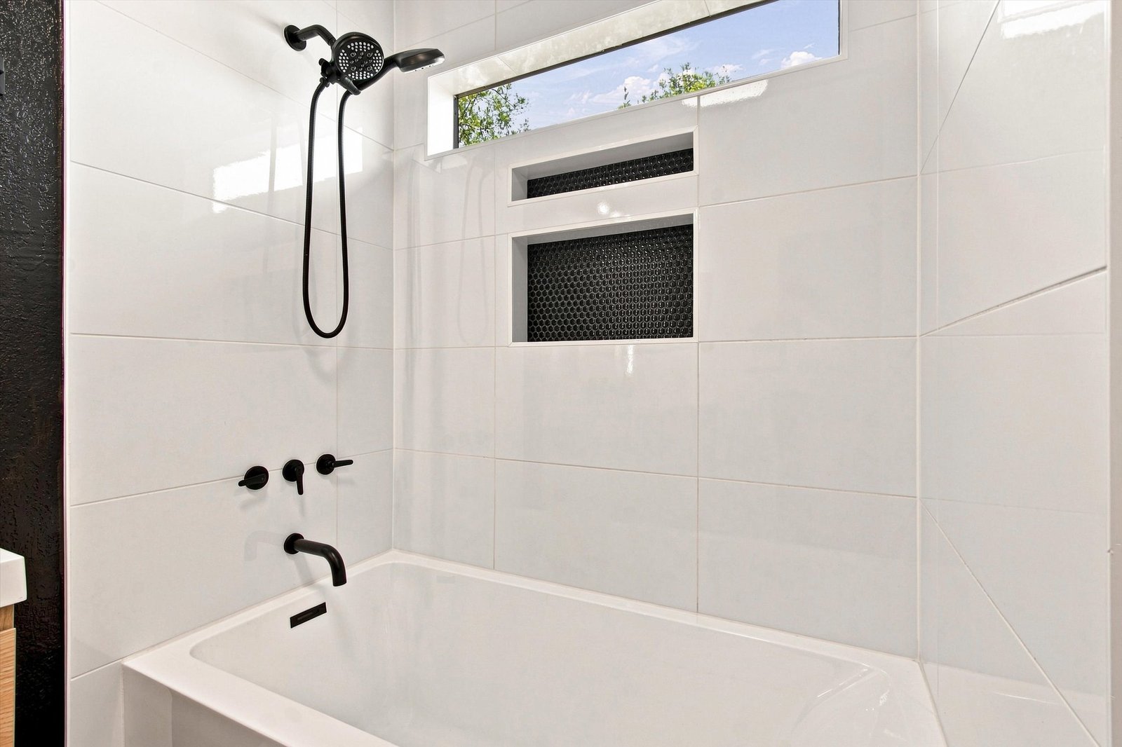 Primary bathroom with white-tiled tub and shower, black penny-tile niche, and matte black fixtures