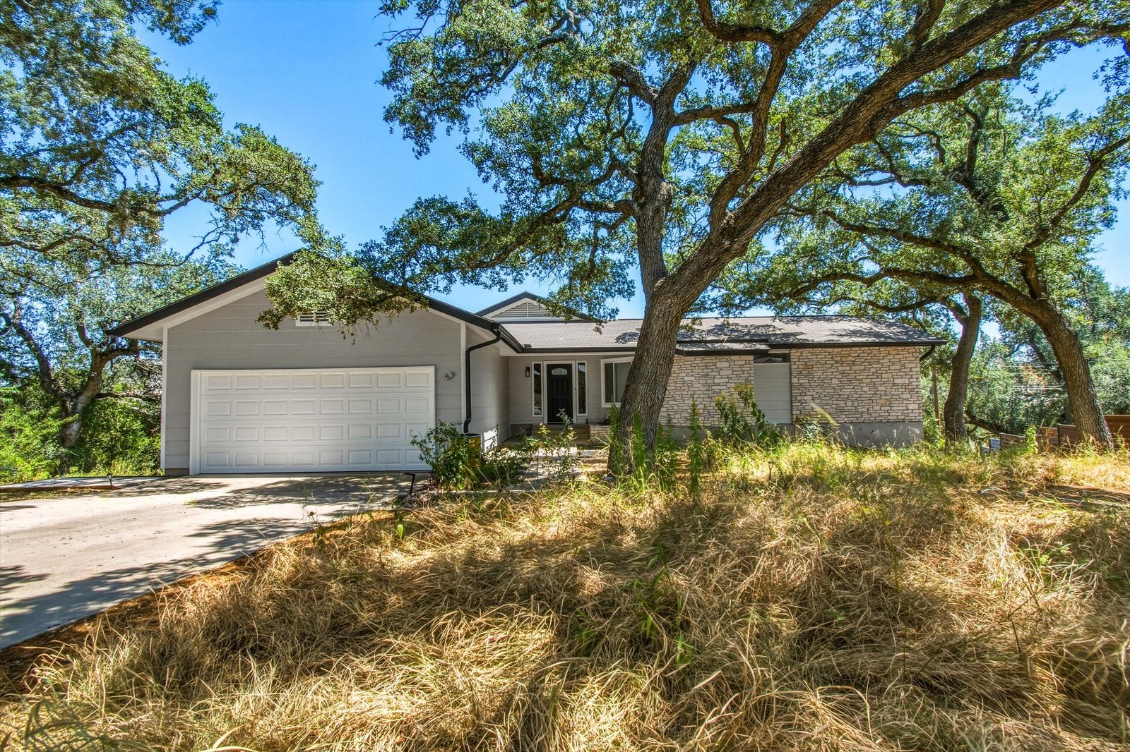 Front elevation with two-car garage and driveway under mature oaks
